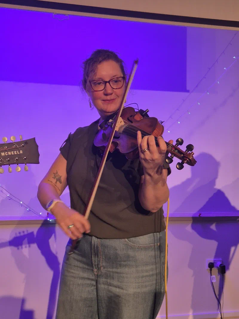 Sarah playing the fiddle under purple stage lighting